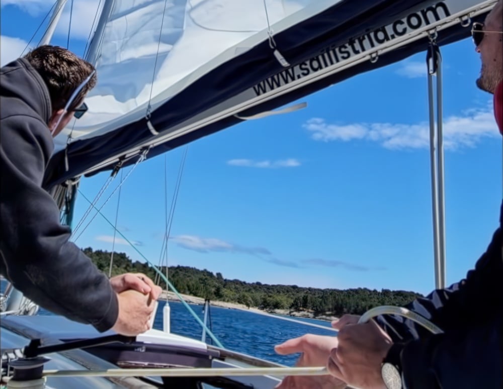 Gosti surađuju i uče upravljati vinčem (winch) tijekom team-building jedrenja s tvrtkom Sail Istria u blizini Pule.