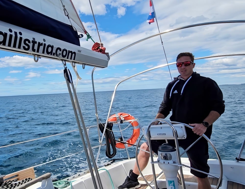 Profesionalni kapetan tvrtke Sail Istria upravlja jedrilicom pod plavim nebom, s vidljivom hrvatskom zastavom.