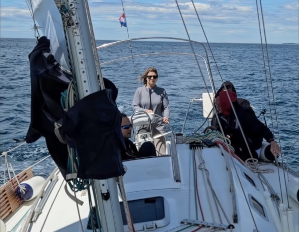 Gošća samopouzdano preuzima kormilo jedrilice Sail Istria, uživajući u iskustvu 'kapetan na jedan dan' u Hrvatskoj.